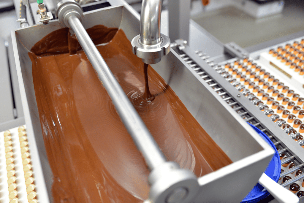 Une femme habillée en uniforme de protection trie du chocolat sur la chaîne de production
